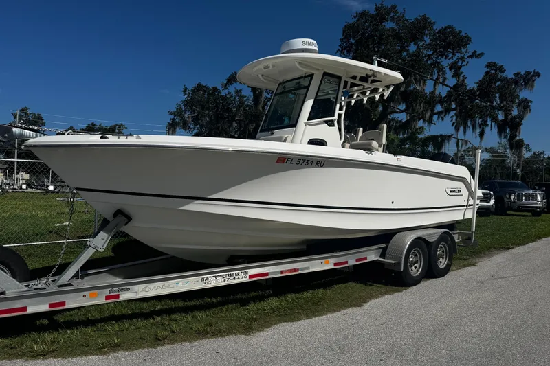 Slide: The Image of 2019 Boston Whaler 26 Outrage boat on trailer, parked outdoors under clear blue sky. - 22
