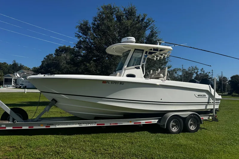 Slide: The Image of 2019 Boston Whaler 26 Outrage boat on trailer, parked on grass under clear blue sky. - 3