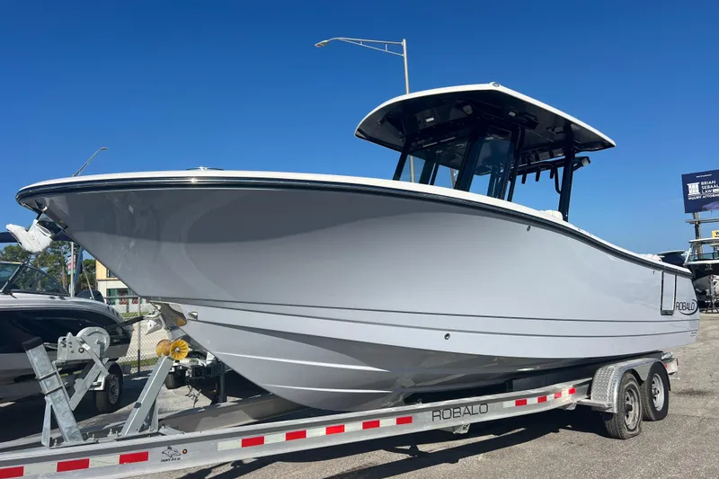 The Image of 2025 Robalo R270 Center Console boat on trailer under clear blue sky. - 0
