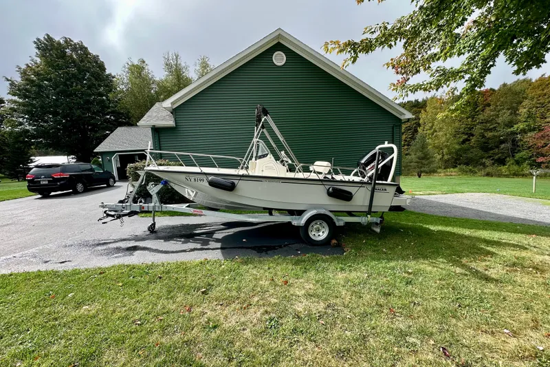 Slide: The Image of 2024 Boston Whaler 170 Montauk boat on trailer, parked near green house. - 2