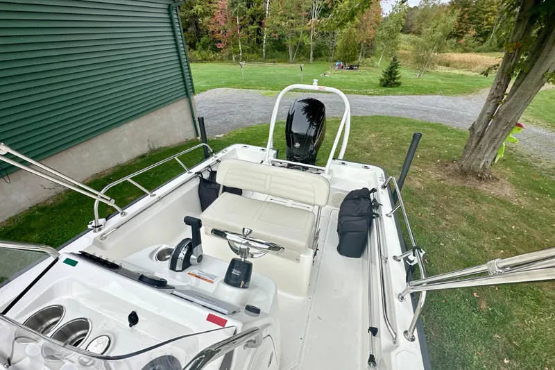 Slide: The Image of 2024 Boston Whaler 170 Montauk boat interior with seating and controls, parked on grass. - 7