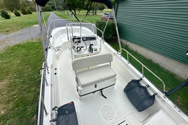 Slide: The Image of 2024 Boston Whaler 170 Montauk boat interior with steering console and seating, parked on grass. - 8