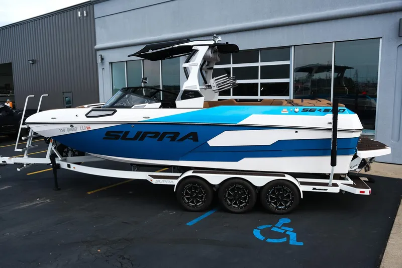 Slide: The Image of 2023 Supra SE550 boat on trailer, blue and white design, parked outside a building. - 3