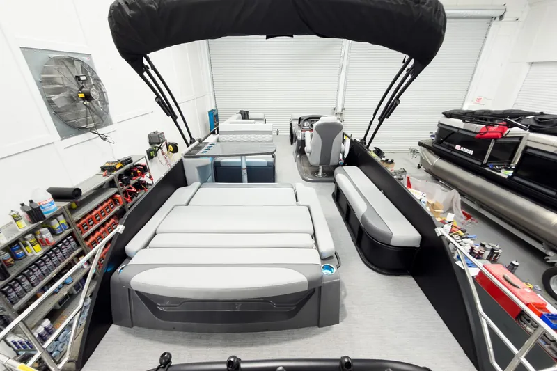 Slide: The Image of 2026 Godfrey Monaco 25' Tritoon with mid-table flip lounge in a workshop setting. - 55