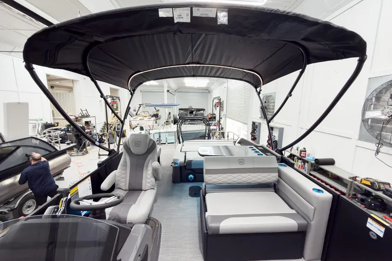 Slide: The Image of 2026 Godfrey Monaco 25' Tritoon with mid-table flip lounge in a workshop setting. - 60