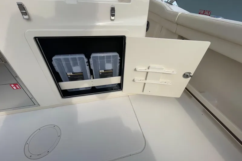 Slide: The Image of 2026 Grady-White Canyon 326 storage compartment with open door and plastic containers. - 19