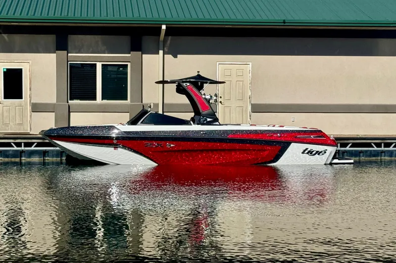 The Image of 2022 Tigé 25ZX boat in vibrant red and white, docked by a building. - 0