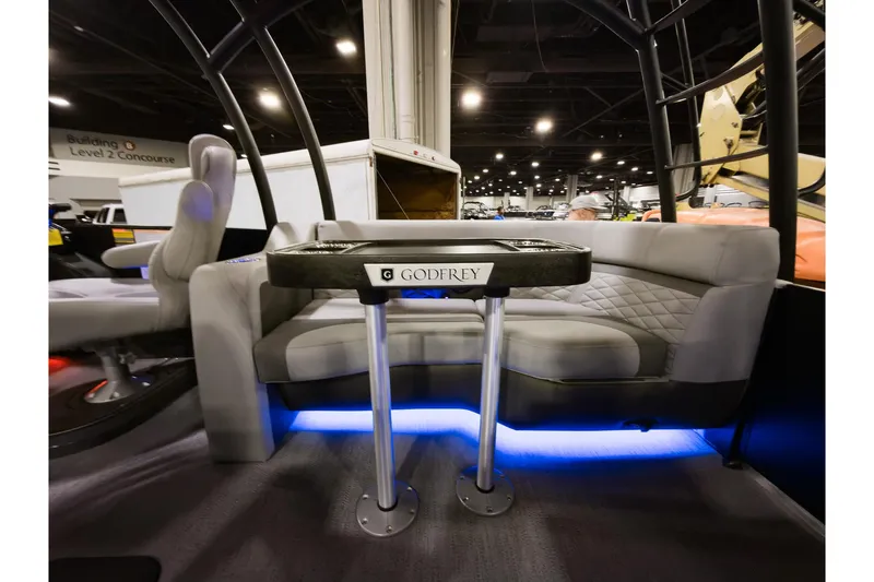 Slide: The Image of 2026 Godfrey Monaco 235 Sun Deck interior with seating and table, illuminated by blue LED lights. - 19