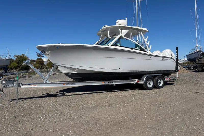 Slide: The Image of 2024 Cobia 280 Dual Console boat on trailer, parked outdoors under clear blue sky. - 16