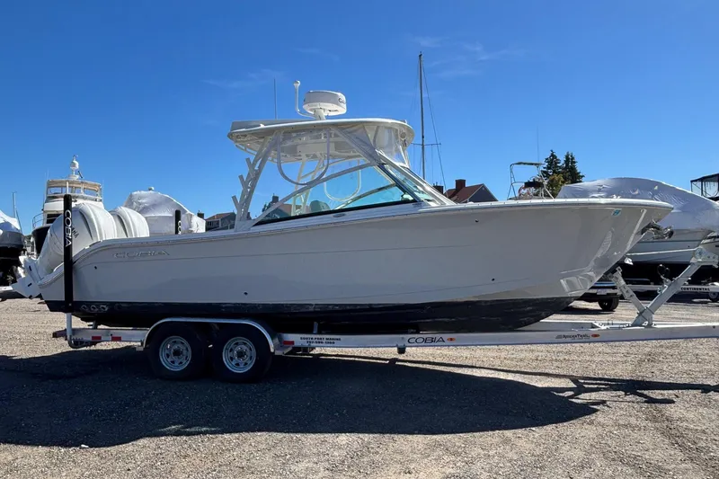 Slide: The Image of 2024 Cobia 280 Dual Console boat on trailer, parked outdoors under clear blue sky. - 19