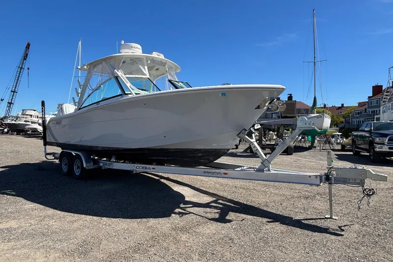 Slide: The Image of 2024 Cobia 280 Dual Console boat on trailer in marina setting. - 20