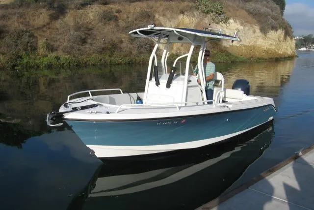 Slide: The Image of 2024 Edgewater 208CC boat on calm water near a rocky shoreline. - 14