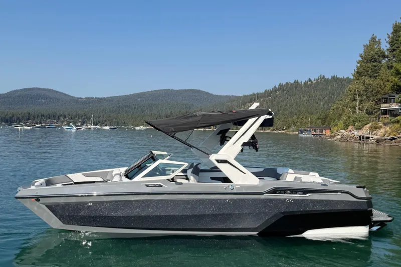 The Image of 2026 MasterCraft XStar 23 boat on a serene lake with forested hills. - 0