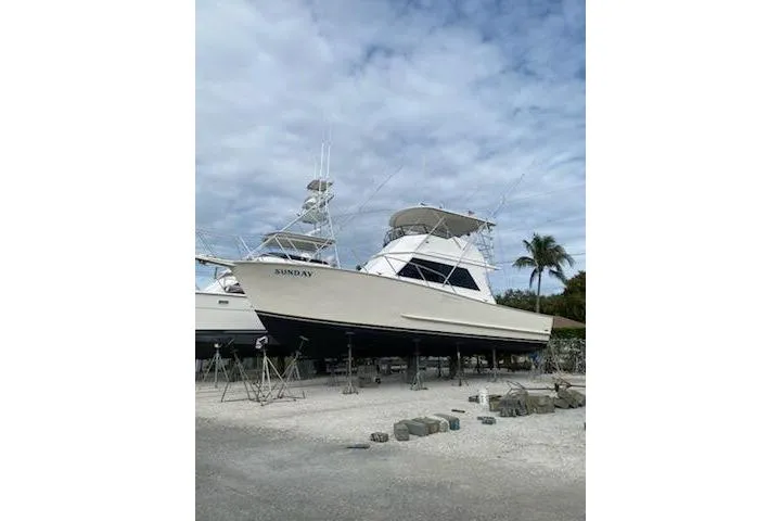 Slide: The Image of 1989 Breaux Brothers 42 Sportfisherman boat on land, under cloudy sky, with palm trees nearby. - 5