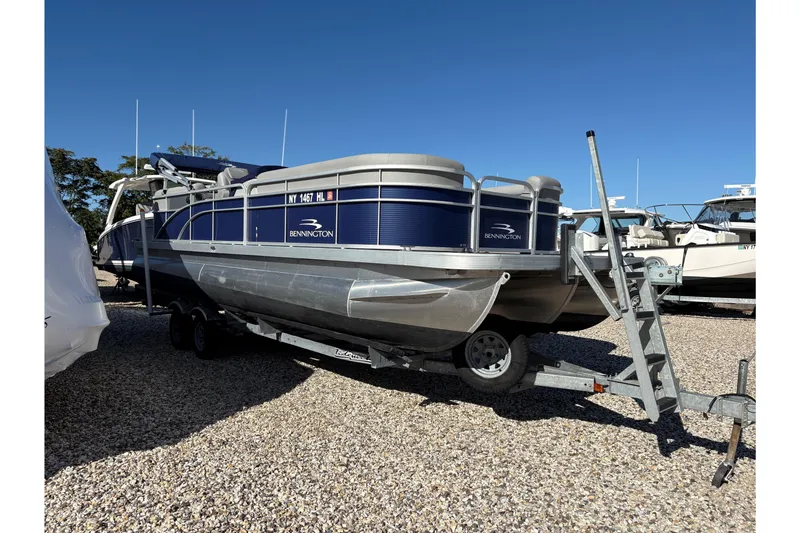 Slide: The Image of 2021 Bennington 24 SVRC pontoon boat on trailer in a gravel lot, surrounded by other boats. - 17