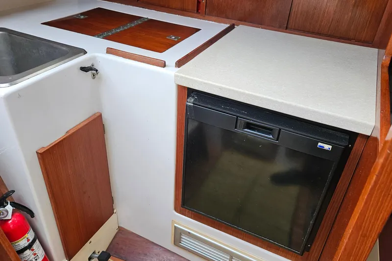 Slide: The Image of 1977 Peterson 34 Sloop galley with sink, fridge, and wooden cabinetry. - 24