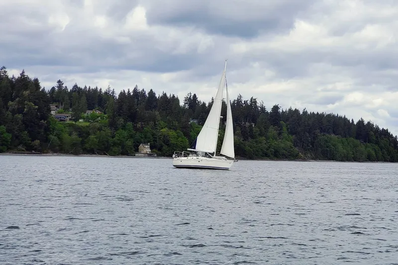 Slide: The Image of Sailboat on calm water near forested shoreline, cloudy sky; 2008 Hunter 49 model. - 13