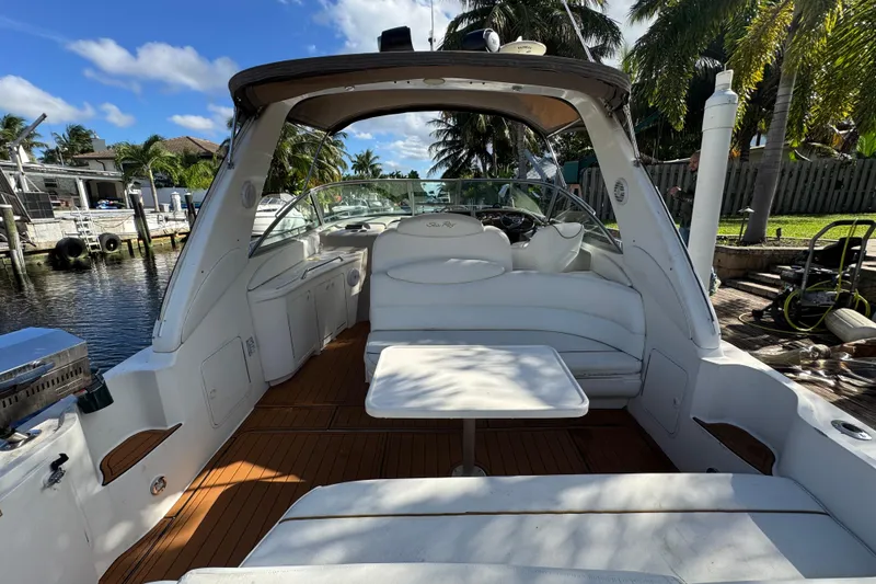 Slide: The Image of 1999 Searay 340 Sundancer boat interior with white seating and table, docked by palm trees. - 2