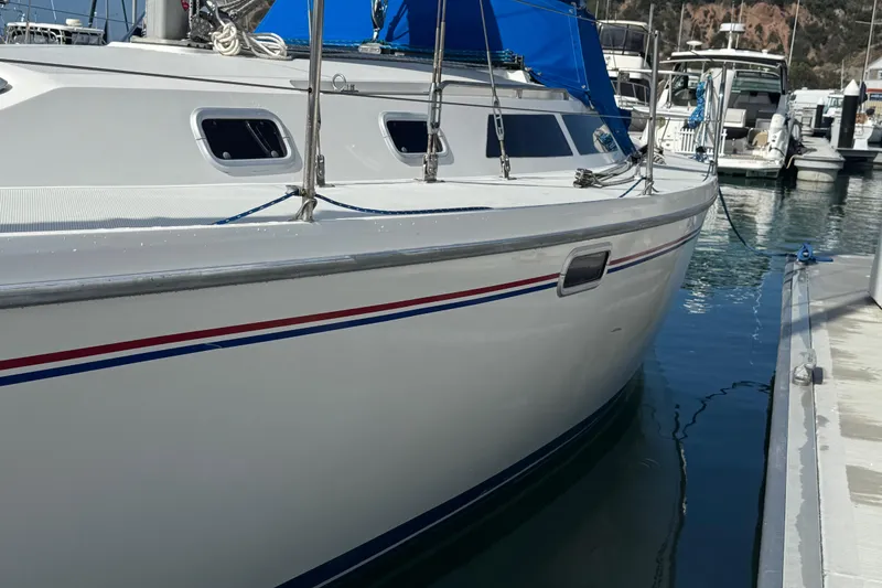 Slide: The Image of 1994 Catalina 320 sailboat docked in marina, featuring sleek white hull and blue accents. - 8