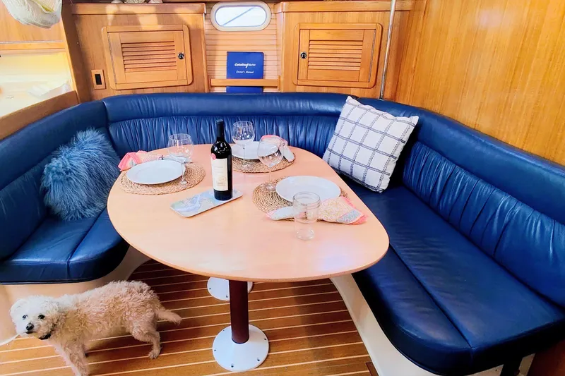Slide: The Image of Cozy dining area in 2003 Catalina 42 MkII yacht with blue seating and a small dog. - 16