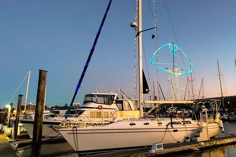 Slide: The Image of 2003 Catalina 42 MkII sailboat adorned with festive lights at a marina during sunset. - 7