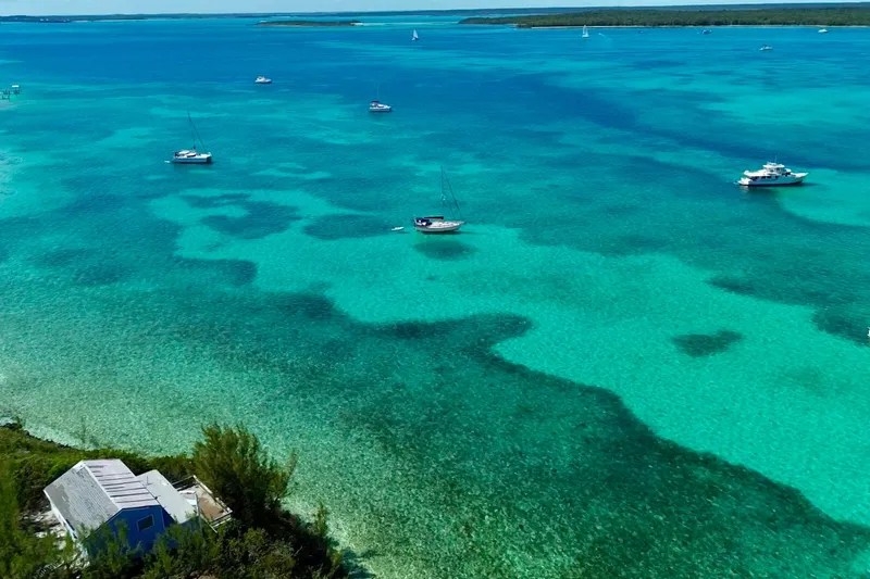Slide: The Image of Turquoise waters with sailboats, including a 1995 Island Packet 40, near a coastal house. - 73