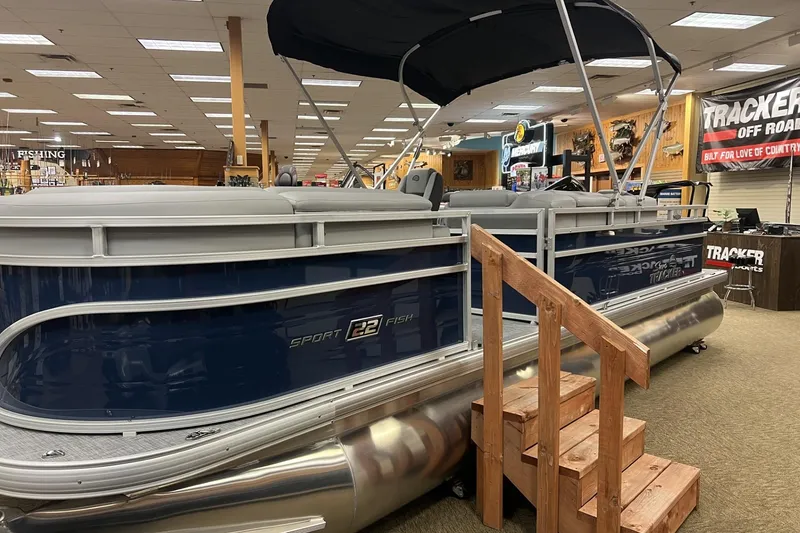 The Image of 2026 Sun Tracker SportFish 22 DLX pontoon boat displayed indoors with wooden steps. - 0