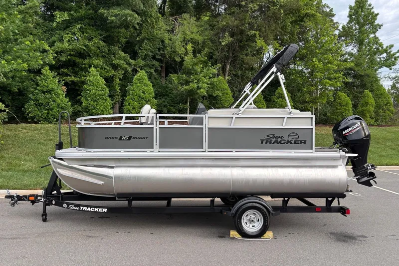 The Image of 2026 Sun Tracker Bass Buggy 16 XL Select pontoon boat on trailer, parked outdoors. - 0
