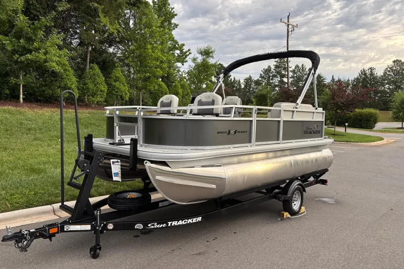 Slide: The Image of 2026 Sun Tracker Bass Buggy 16 XL Select pontoon boat on trailer, parked outdoors. - 2