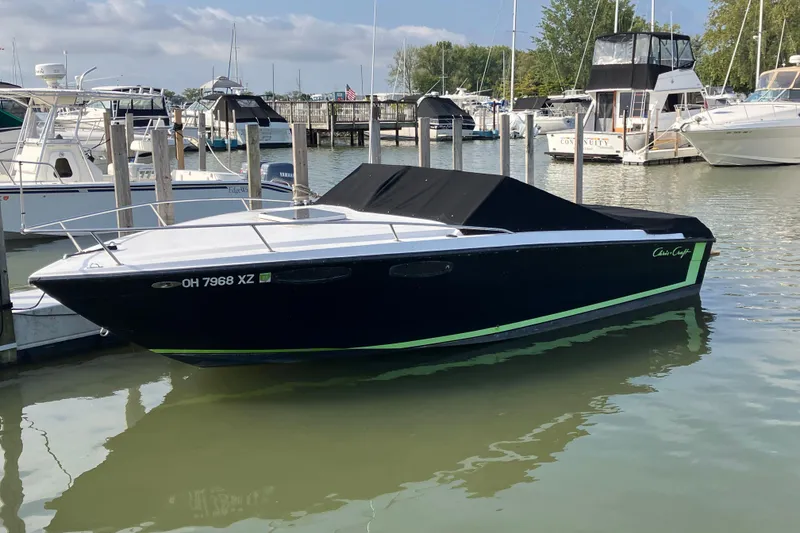 The Image of 1983 Chris-Craft 230 Scorpion boat docked in marina, black hull with green accents. - 0