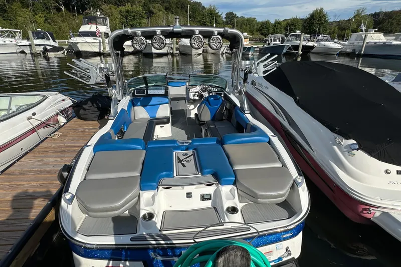 Slide: The Image of 2016 MasterCraft X23 boat docked, featuring blue and gray seating, surrounded by other boats. - 2