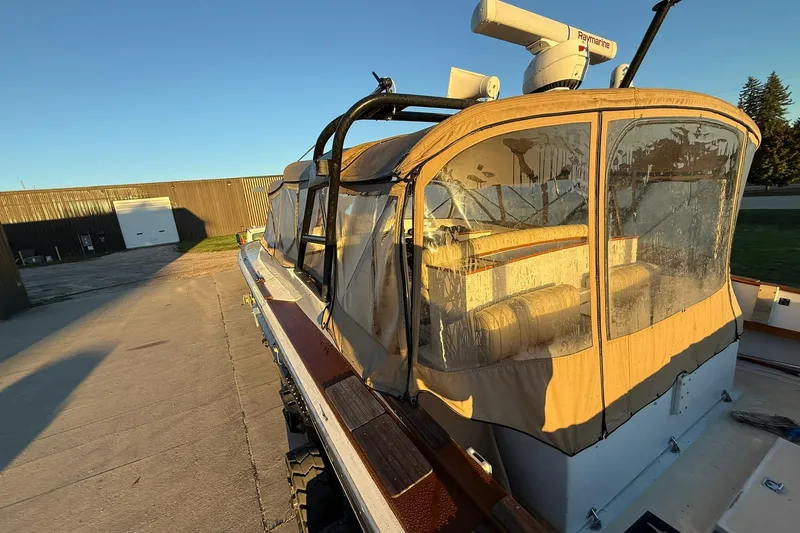 Slide: The Image of 1979 Magnum 38 Sport boat with tan canopy, parked on concrete under clear blue sky. - 50