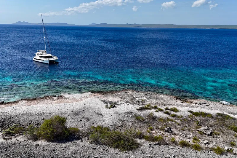 Slide: The Image of Sailboat Leopard 42 anchored near rocky shore with clear blue ocean, 2023. - 103