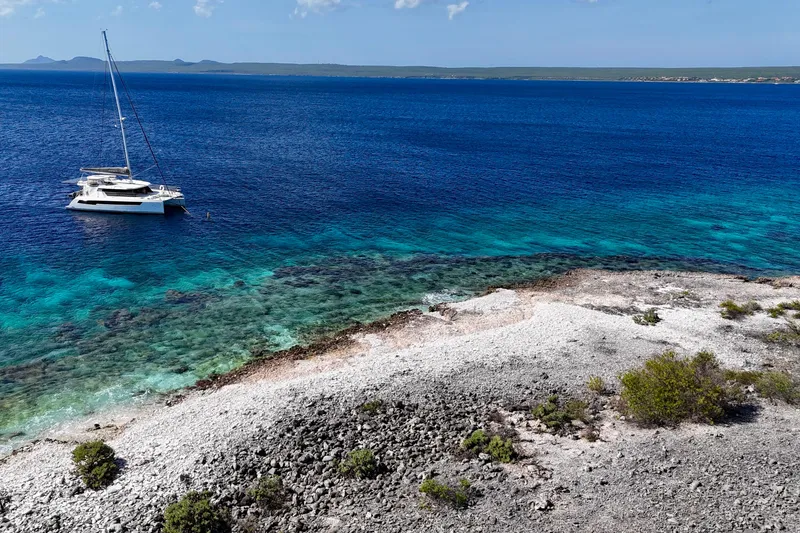 Slide: The Image of A Leopard 42 catamaran anchored near a rocky shoreline with clear blue waters, 2023. - 105
