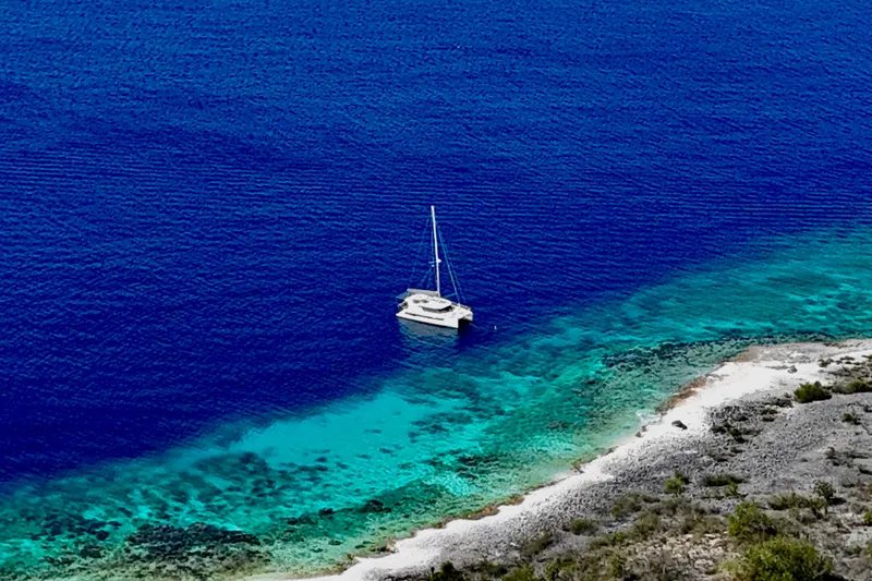 Slide: The Image of Sailboat Leopard 42 (2023) anchored in clear blue waters near a rocky shoreline. - 106