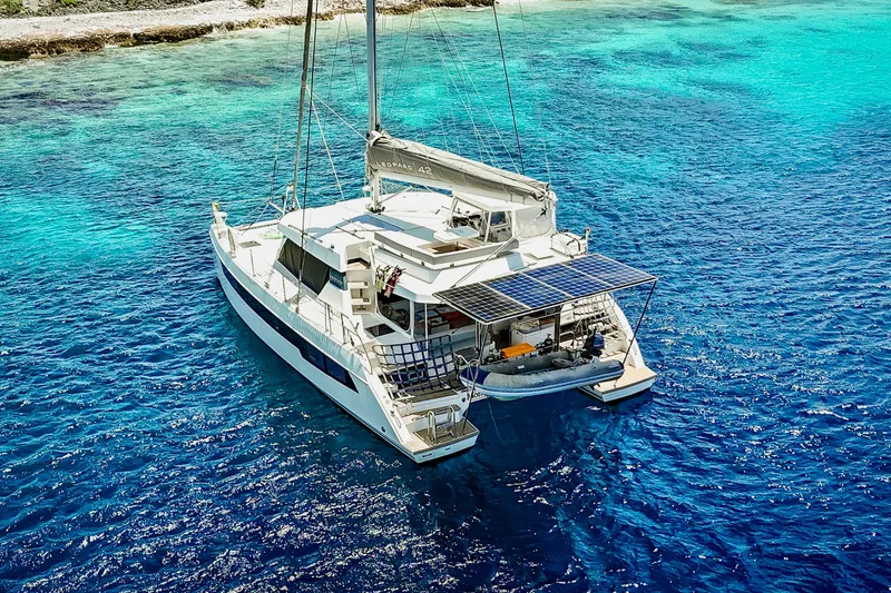 Slide: The Image of 2023 Leopard 42 catamaran sailing in clear blue waters near a rocky shoreline. - 11