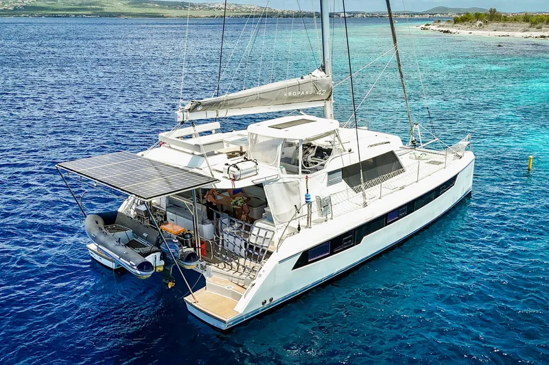 Slide: The Image of 2023 Leopard 42 catamaran anchored in clear blue waters, featuring solar panels and a small dinghy. - 14