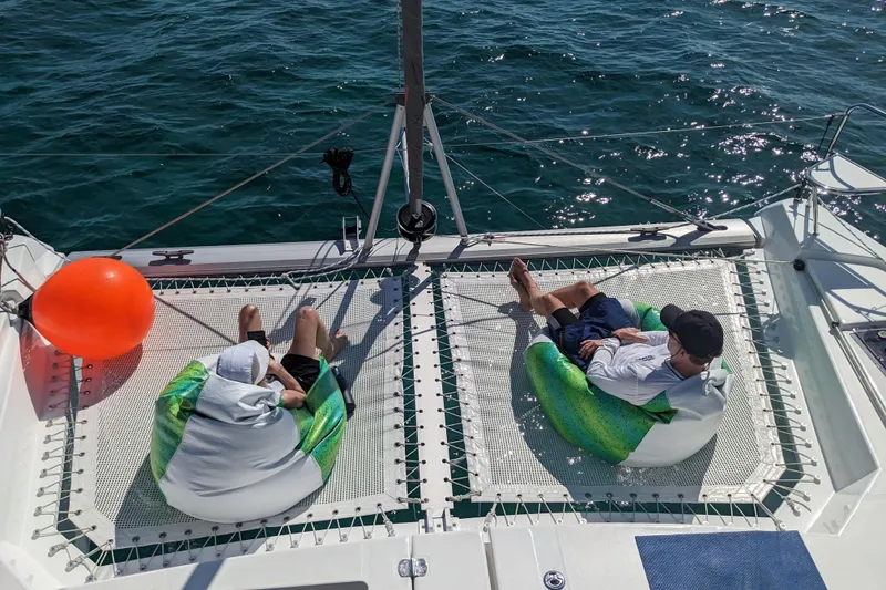 Slide: The Image of Two people relaxing on a 2023 Leopard 42 catamaran netting over the ocean. - 24