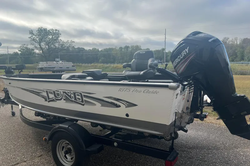 Slide: The Image of 2016 Lund 1875 Pro Guide boat with Mercury engine on trailer, parked outdoors. - 2