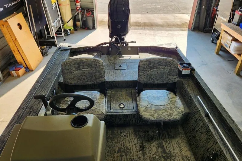Slide: The Image of 2026 Tracker Grizzly 1754 SC boat interior with camouflage seats in a garage setting. - 5