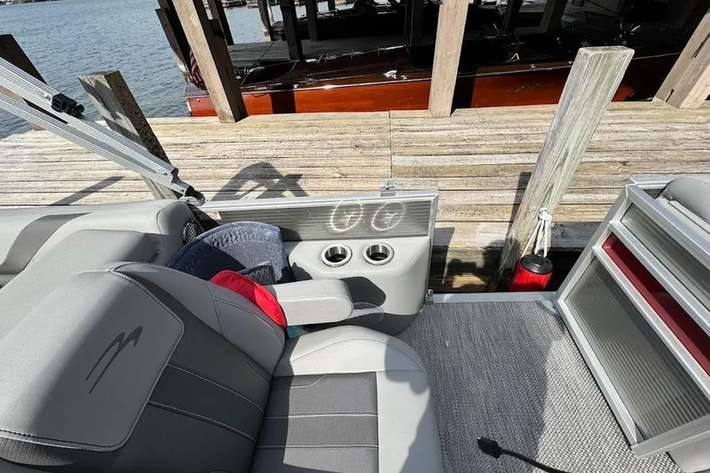 Slide: The Image of 2024 Bennington 22 SSRX boat interior with steering wheel and seating, docked by a stone wall. - 11