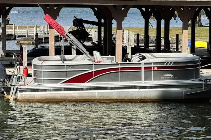 Slide: The Image of 2024 Bennington 22 SSRX pontoon boat with red-covered seats docked by a wooden pier. - 2