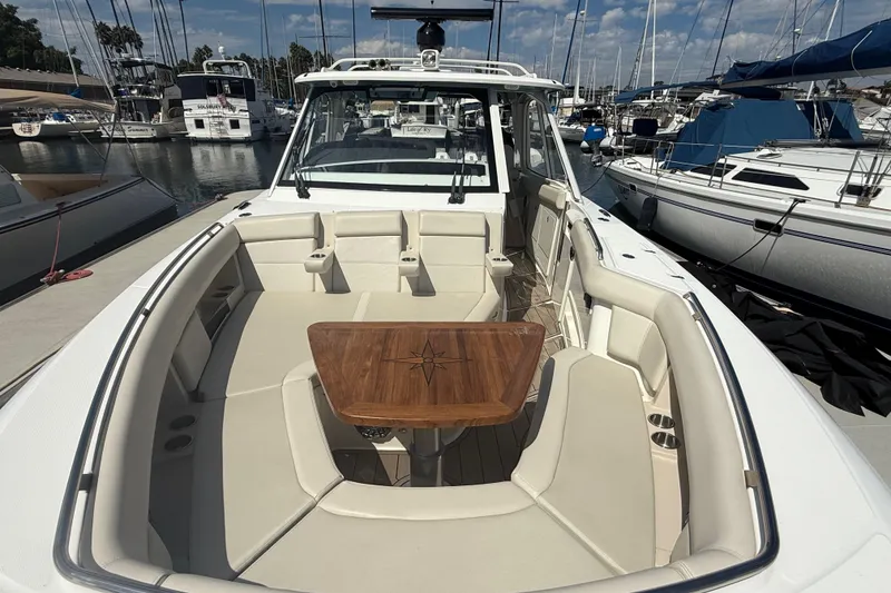 Slide: The Image of 2023 Boston Whaler 380 Realm boat interior with seating and wooden table, docked at marina. - 20