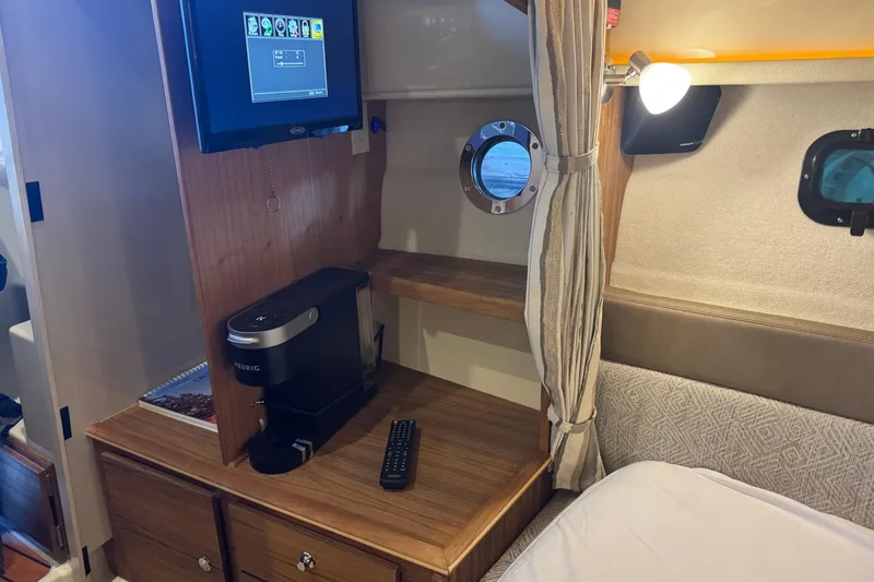 Slide: The Image of 2025 Ranger Tugs R-27 cabin interior with TV, coffee maker, and porthole window. - 18