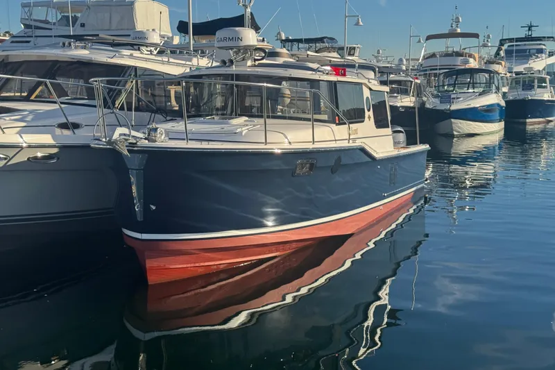 Slide: The Image of 2025 Ranger Tugs R-27 boat docked in a marina, reflecting on calm water. - 4
