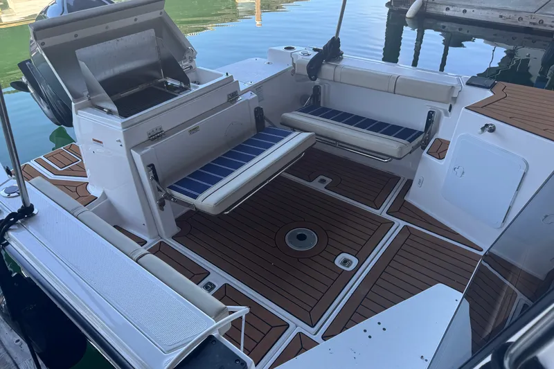 Slide: The Image of 2025 Ranger Tugs R-27 boat interior with seating and grill, docked on calm water. - 8