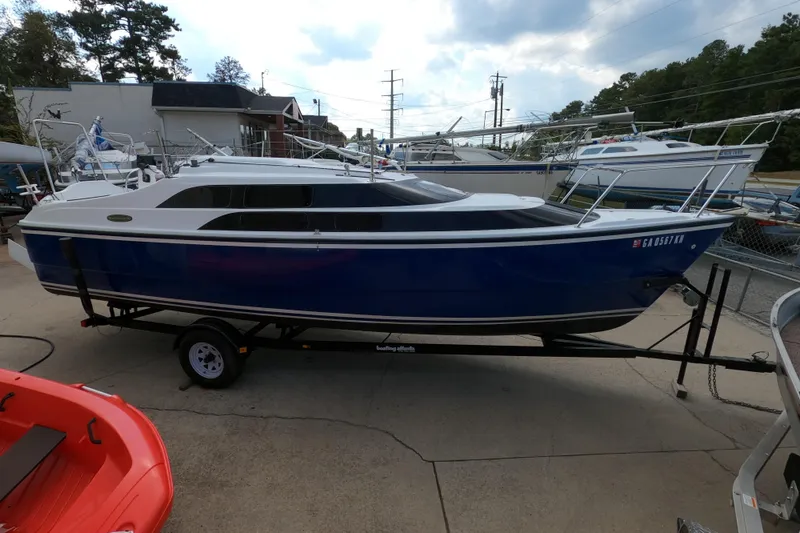 Slide: The Image of 2007 MacGregor 26M sailboat on trailer, blue hull, parked outdoors. - 23