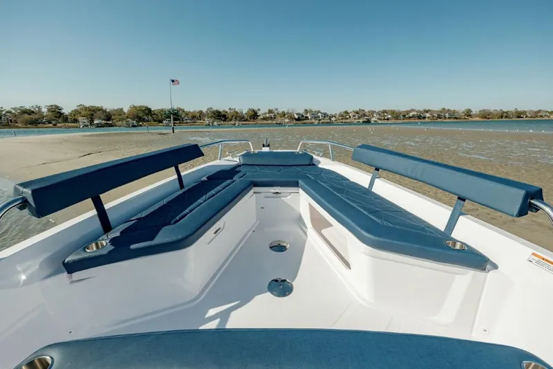 Slide: The Image of 2025 Axopar 29 Sun Top boat with blue seating, docked by a sandy shore. - 7