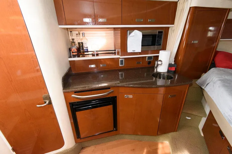 Slide: The Image of 2012 Sea Ray 330 Sundancer interior kitchen with wood cabinetry, microwave, and sink. - 17