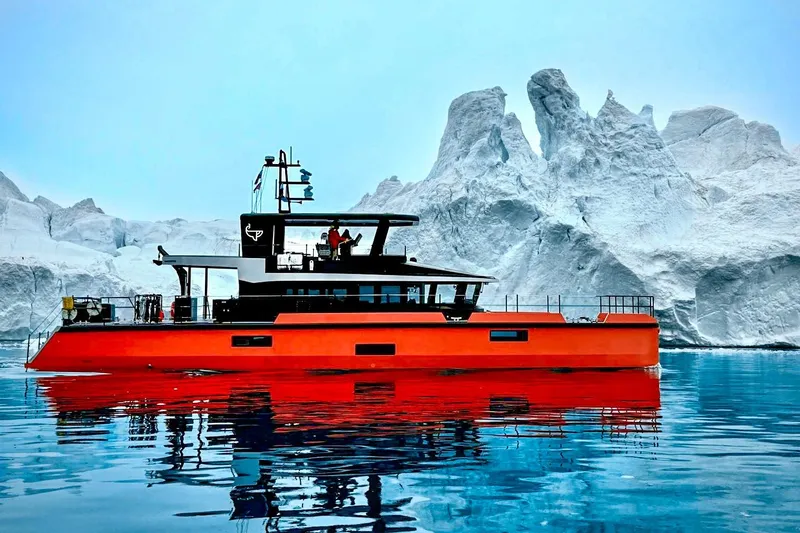 The Image of 2023 Naval Yachts XPM 78 in icy waters, vibrant orange hull, majestic iceberg backdrop. - 0